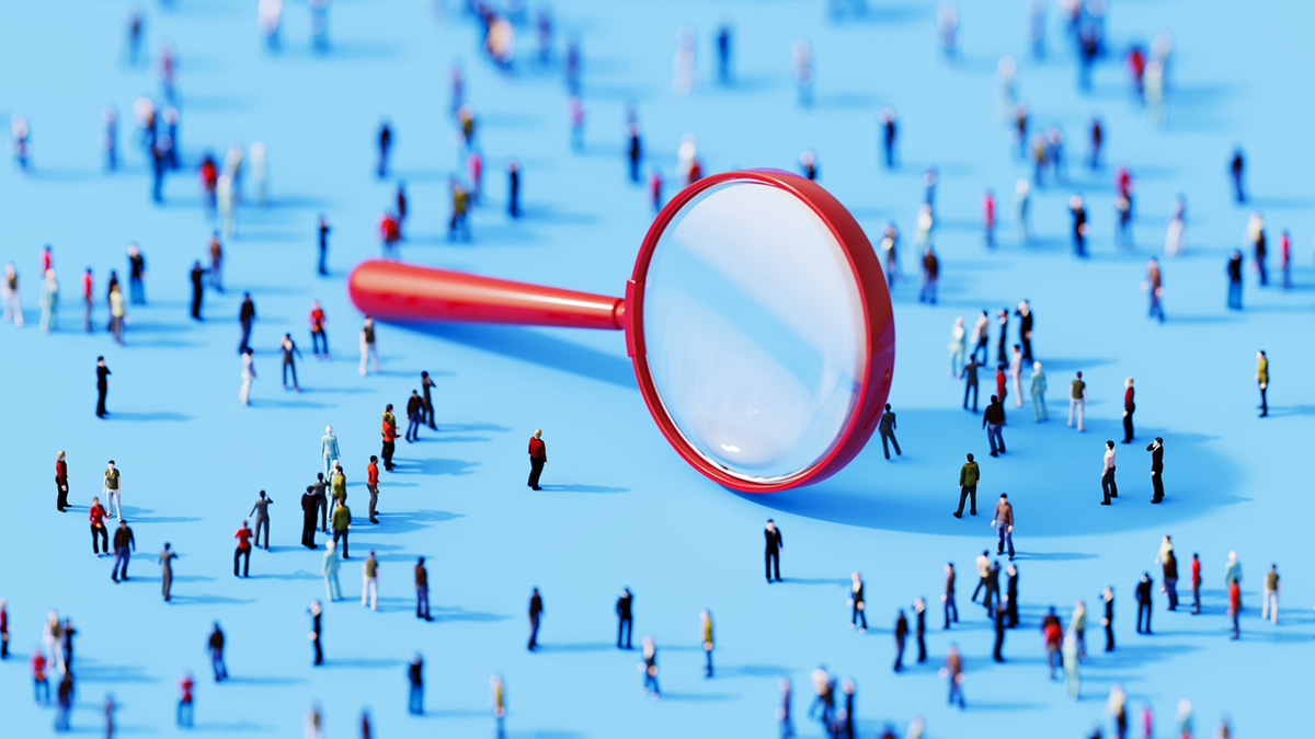 A large red magnifying glass lies on a bright blue surface surrounded by numerous tiny figurines of people.