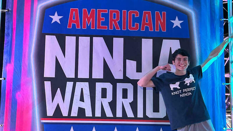 Brown haired boy poses in front of American Ninja Warrior sign