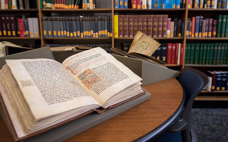 A Medieval book lays open on a table in a library.
