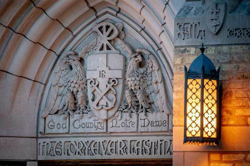 Stone carving above a doorway at the University of Notre Dame featuring two eagles flanking a shield with a cross and anchor, with the words 